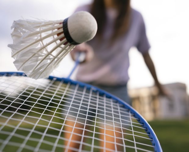 Close-up of a badminton racket hitting a shuttlecock outdoors.
